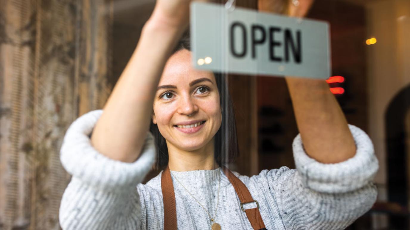Woman coffee shop owner putting an open sign on the front door.