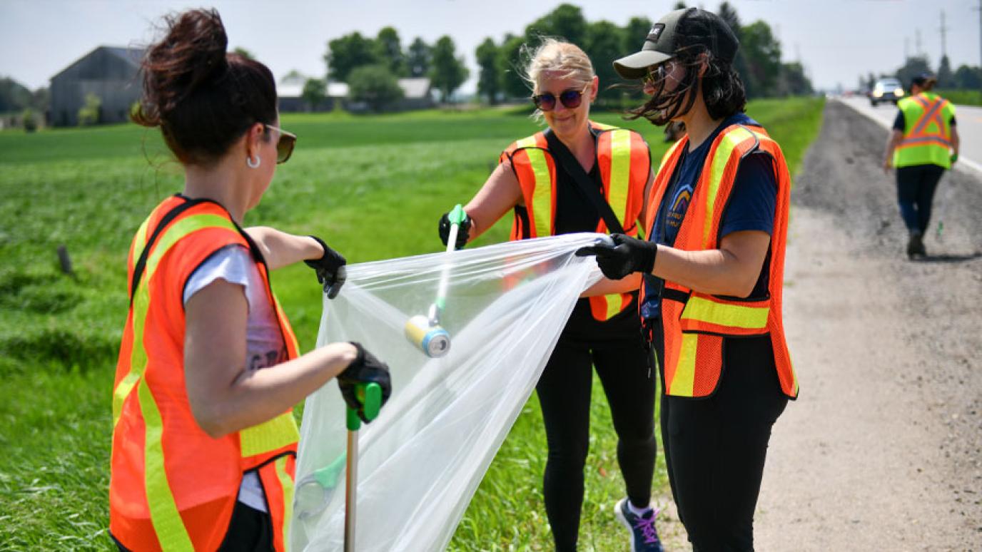 Employees in safety vest pick up garbage at the side of the road as part of Public Works week