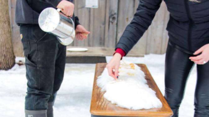 two people pouring maple syrup over snow