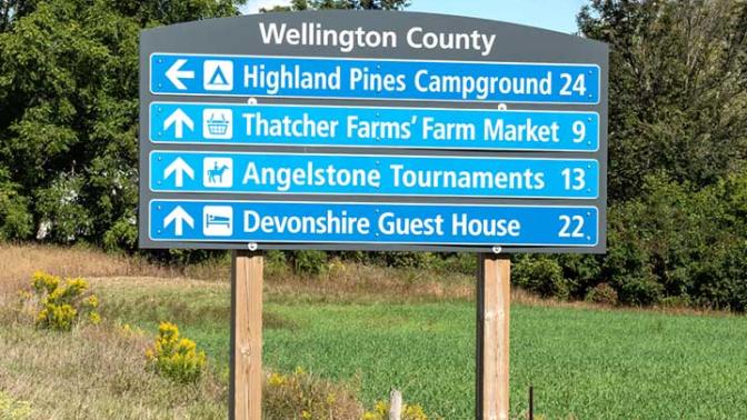 Wellington County blade signs mounted at the side of the road, listing local businesses and distance to them
