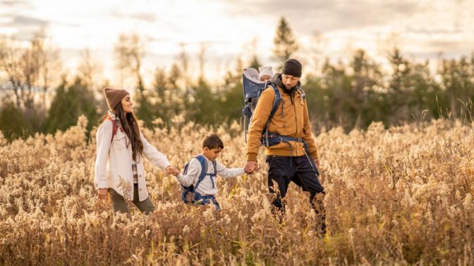 A young family of four hike their way through the tall grass on a cool fall day.