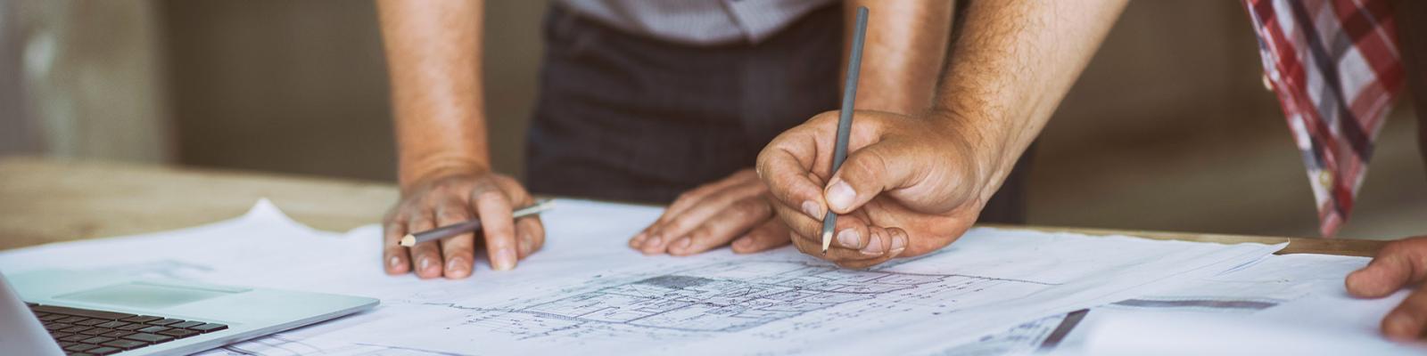 Cropped view of two peoples hand working at a desk making notes on architectural plans