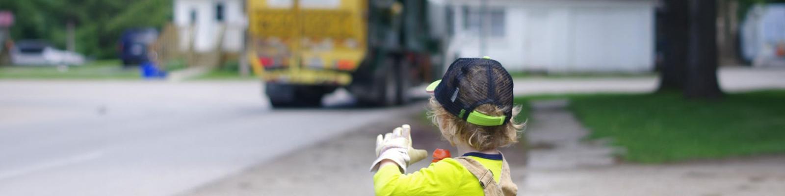 Boy in yellow shirt and waving at garbage truck in the distance on a quiet residential street