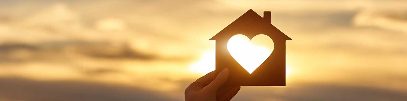 A wooden cutout in the shape of a house with a heart shape cut out of the centre